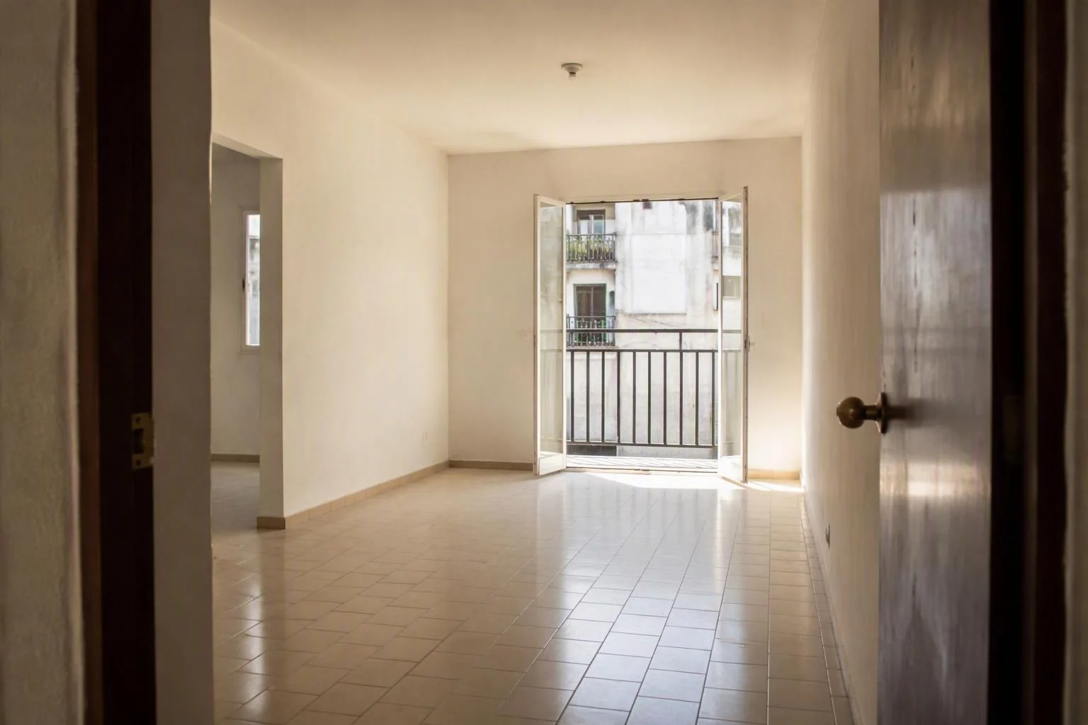 Departamento vacío con puerta de balcón abierta y piso de mosaico